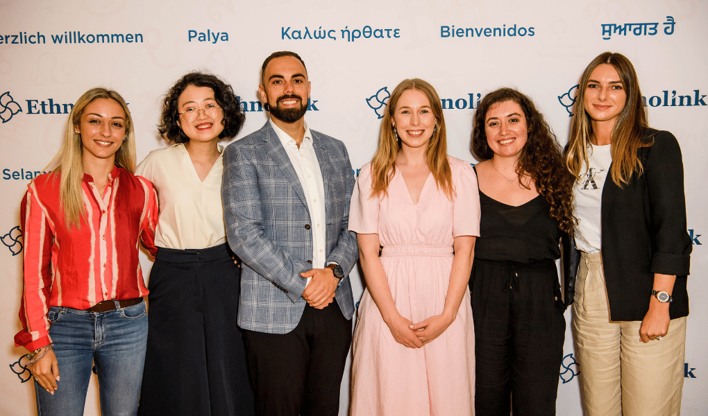 The Ethnolink team stands, smiling, in front of a media wall at CULTURELINK 2023. From left to right, Fabiana Franco, Emily Tan, Costa Vasili, Rachael Coulthard, Ana Barciela, and Cloé Bru.